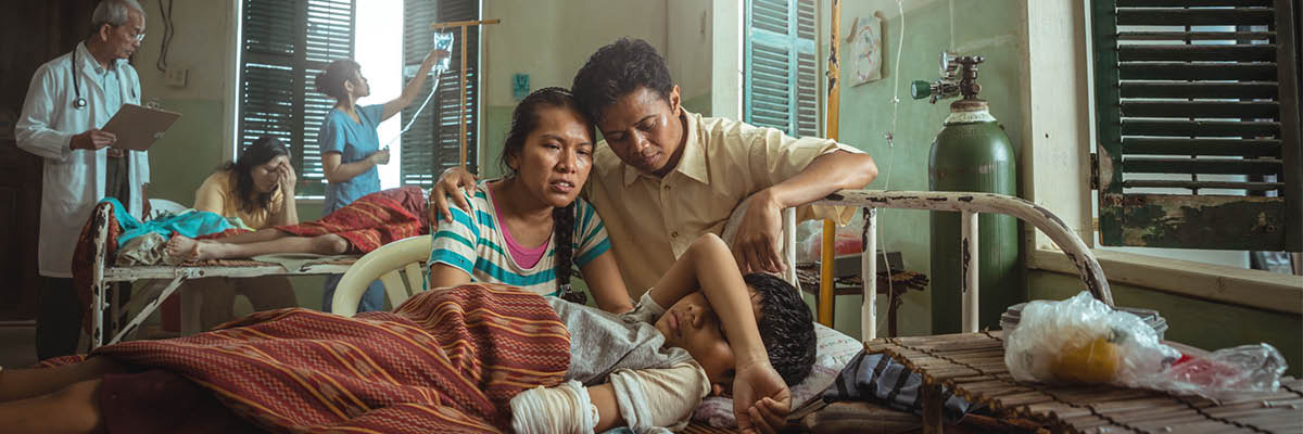 ဆေးရုံခုတင်ပေါ်က ကလေးဘေးမှာ မိဘတွေ စိုးရိမ်တကြီး ထိုင်နေ။