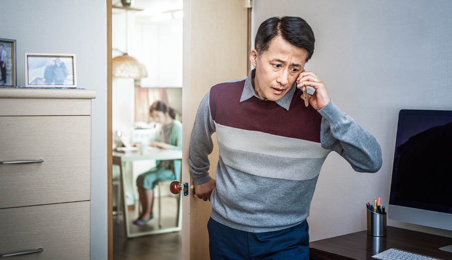 Zborový starší telefonuje a zatvára dvere do miestnosti, kde si jeho manželka študuje