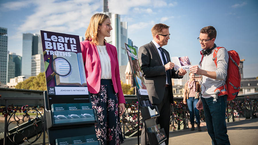 Jehovovi svedkovia pri stojanoch s biblickými publikáciami hovoria s mužom