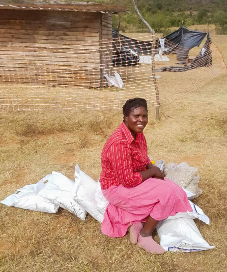 Prisca akiwa nje ya nyumba yake, akitabasamu huku akiwa na mifuko kadhaa ya misaada ya chakula.