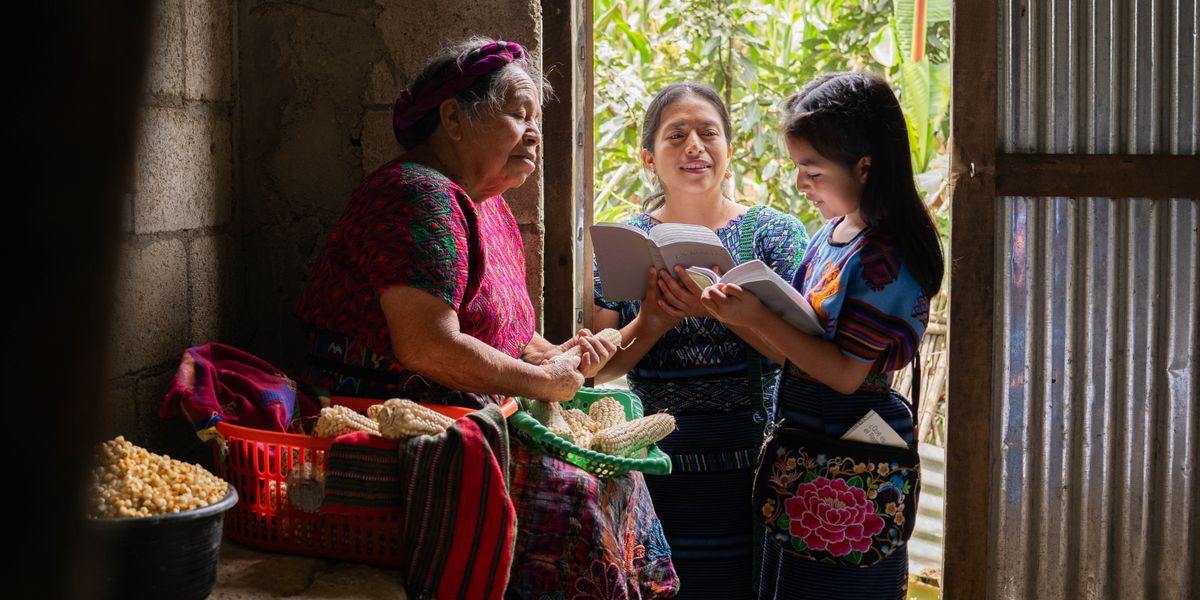 Msichana Shahidi na mama yake wakisoma andiko pamoja na mwanamke anayepukuchua mahindi nyumbani kwake.