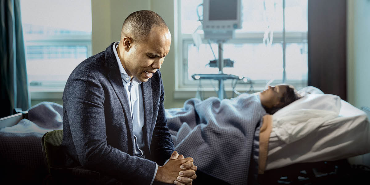Ndugu akisali kwa ajili ya mke wake mgonjwa, aliyelala kwenye kitanda cha hospitali.