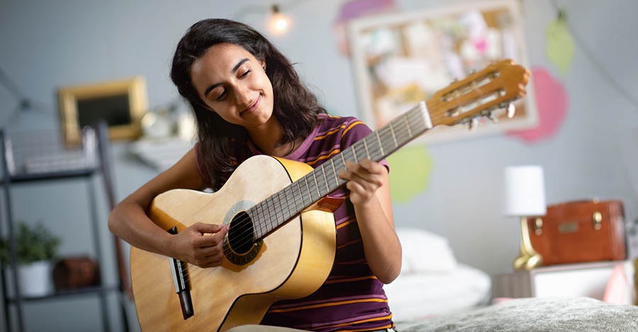 Genç kız yatak odasında gitar çalıyor.