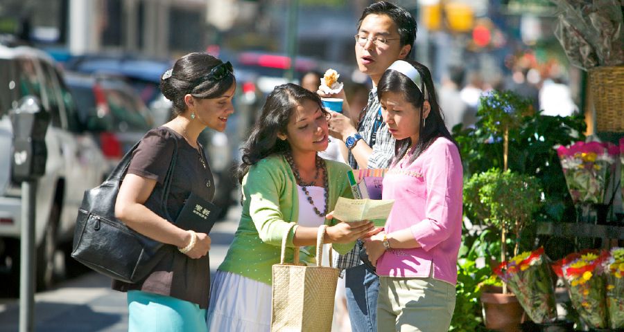 Two sisters de preach to one young woman for street. One young man de check to see wetin them de talk about.