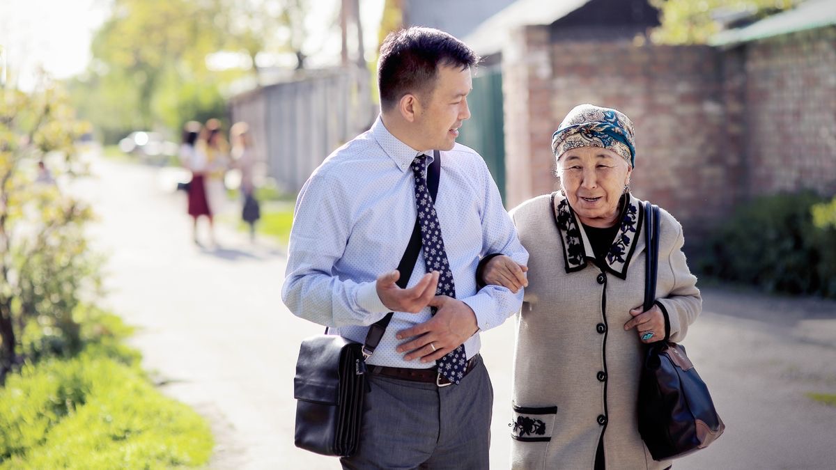 One young elder de use e hand support one old sister as them de waka together for preaching.