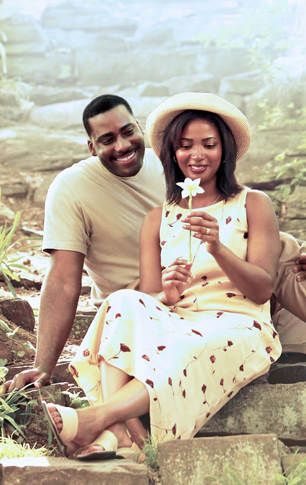 A husband and wife sitting in a garden, looking at a flower