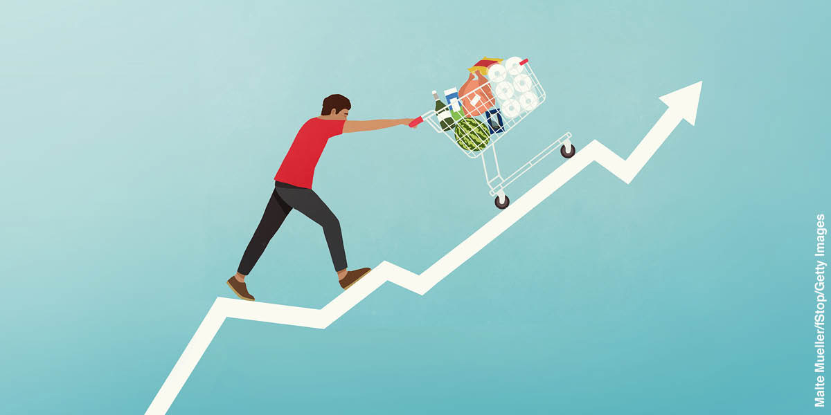 Graf menunjukkan harga barang meningkat dengan cepat. Di atas garisan graf itu, seorang lelaki sedang menolak troli yang penuh dengan barangan.