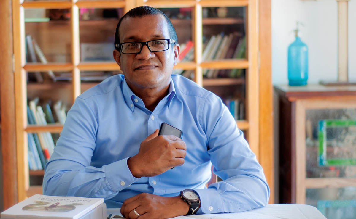Argenis jókòó sídìí tábìlì rẹ̀, ó mú fóònù, Bíbélì àti ìwé “Gbádùn Ayé Rẹ Títí Láé!” dání
