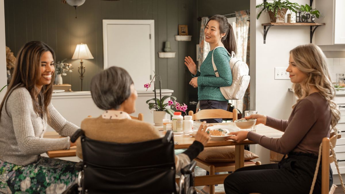 Two sisters visiting an elderly sister in her home. Her caregiver joyfully waves to them as she walks toward the door.