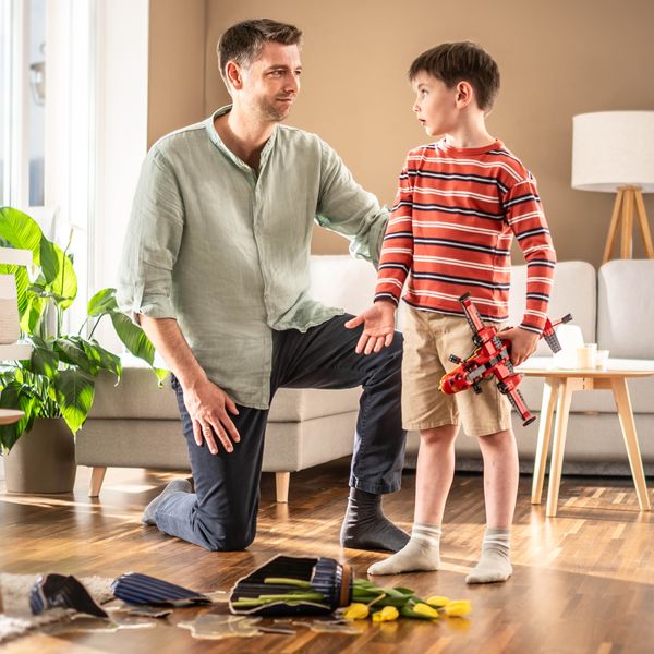 A father patiently listening to his young son as the boy explains how he accidentally broke a flower vase while playing with a toy plane.